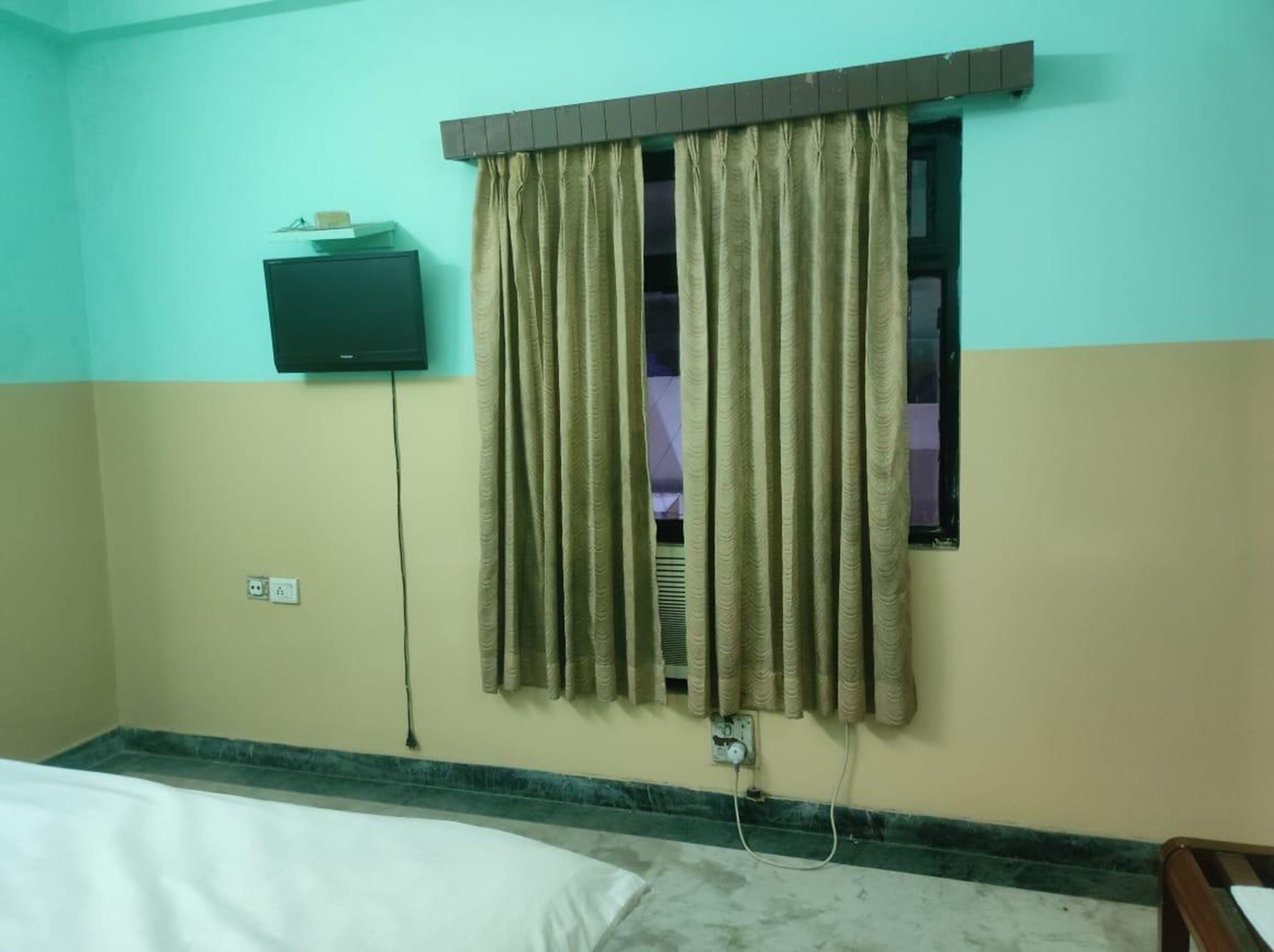 A hotel room with a bed, a television mounted on the wall, and a window with curtains.