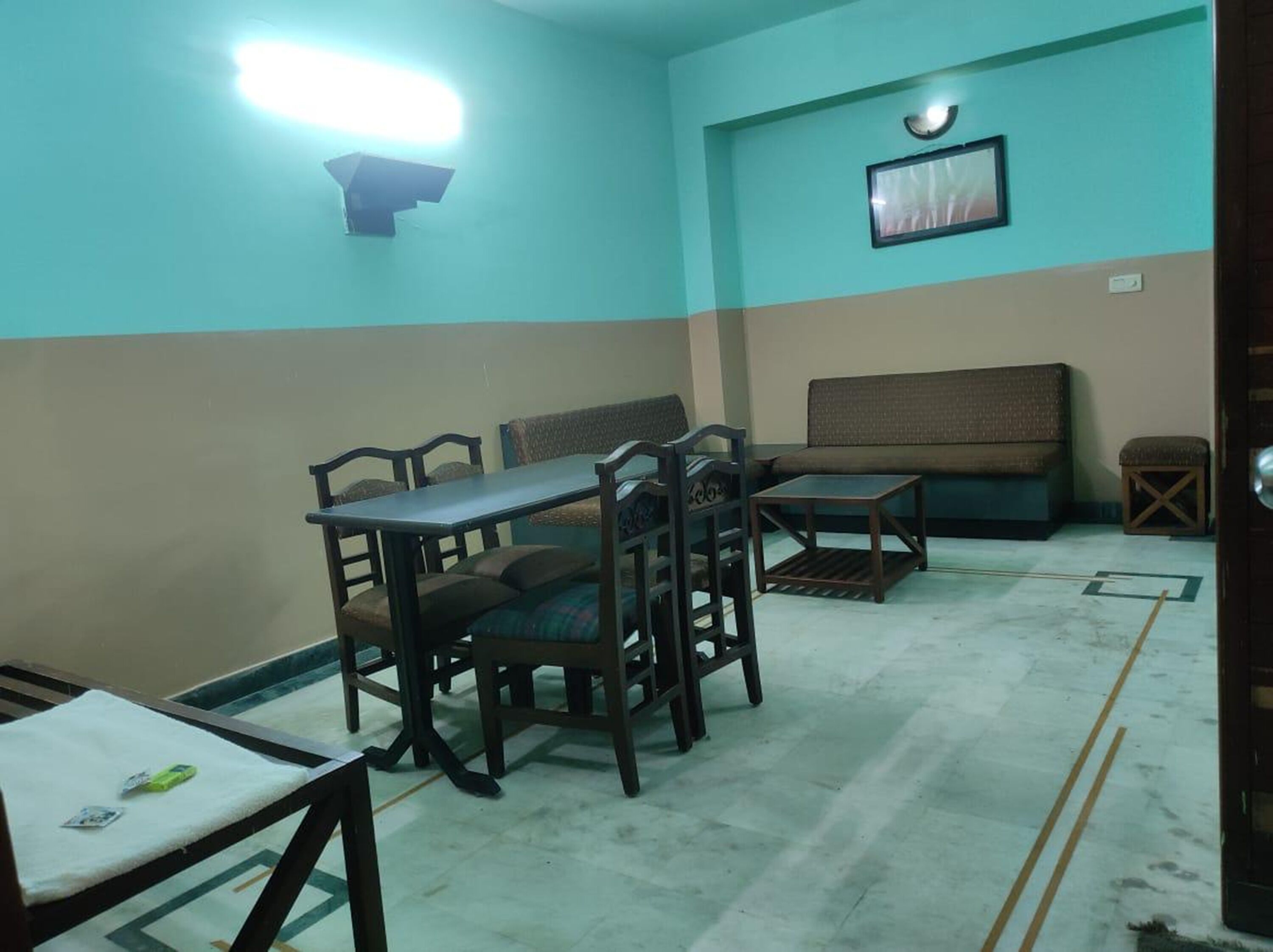 A room with a dining table and chairs, a sofa, and a small stool.