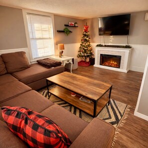 A living room with a brown sofa, a wooden coffee table, a fireplace, a TV, and a Christmas tree. - Mountains | HotTub | Sauna | Wineries | Hikes (Mount Jackson)