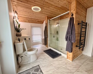Un baño con inodoro, bidé, cabina de ducha de vidrio, paredes de madera y un perchero para toallas.