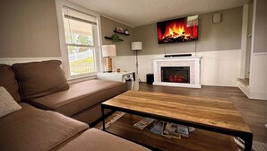 En stue med sofa, sofabord, pejs og tv hængt på væggen.