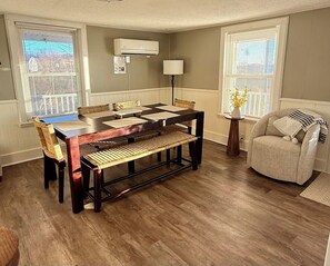 Una zona de comedor con una mesa y sillas de madera, una lámpara y un sillón con cojín.