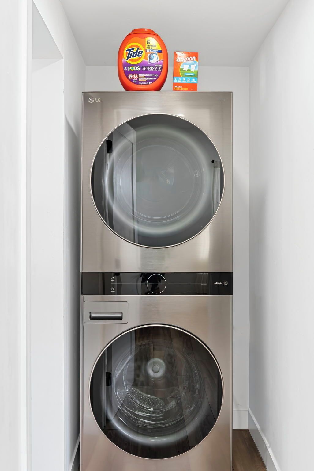 A stainless steel wall-mounted washer and dryer unit with a control panel and a small storage compartment.
