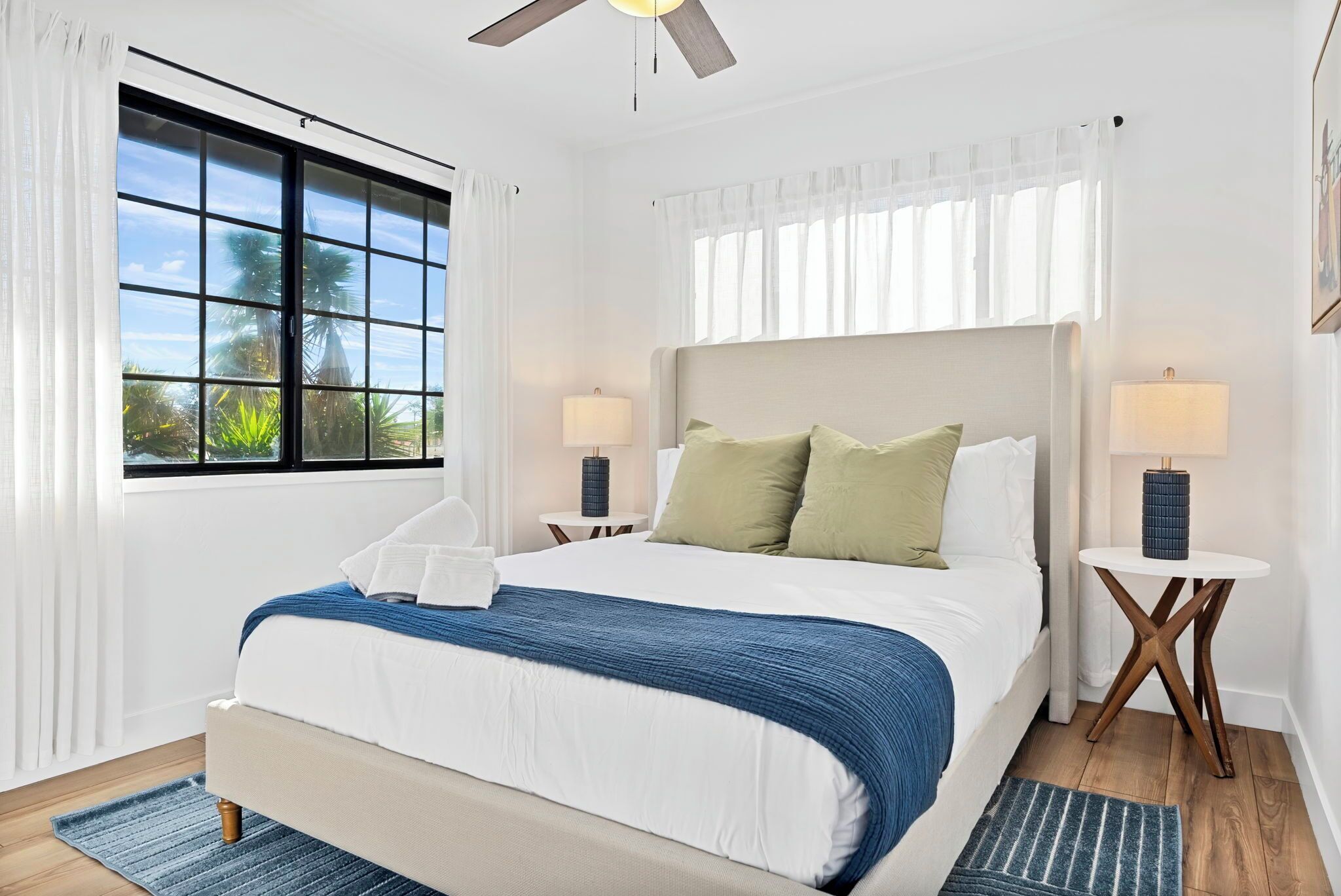 A bedroom with a large bed, two bedside tables with lamps, a ceiling fan, and a window with curtains.