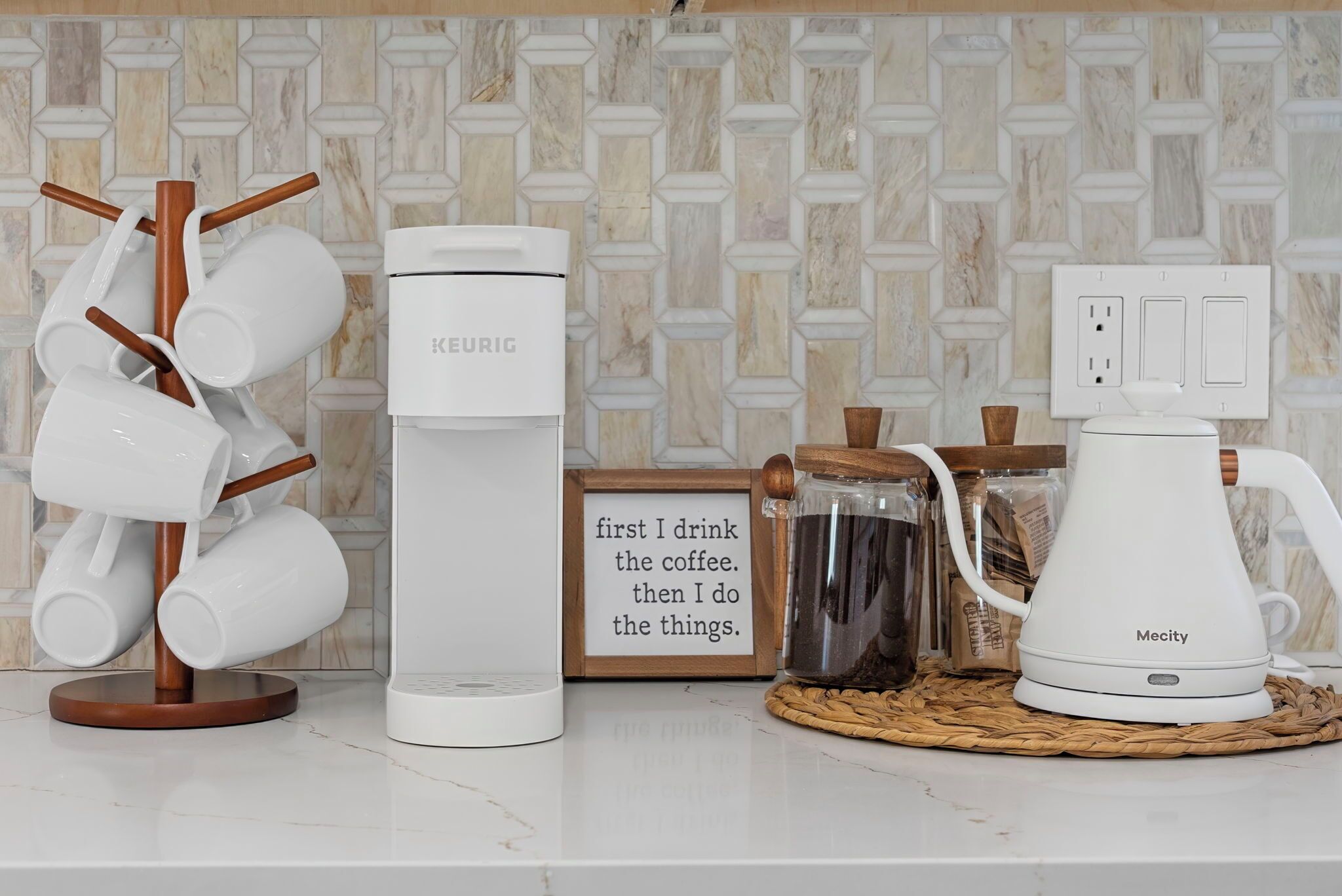 A kitchen counter with a coffee maker, a mug rack, a framed quote, and a kettle.