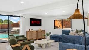Moderni olohuone, josta on näkymä uima-altaalle, seinällä Netflixin logo, sininen sohva ja rottinkikori.