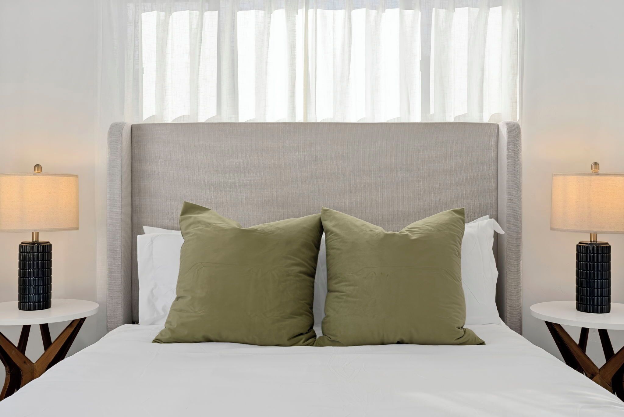 A hotel room with a large bed, two bedside tables with lamps, and sheer curtains.