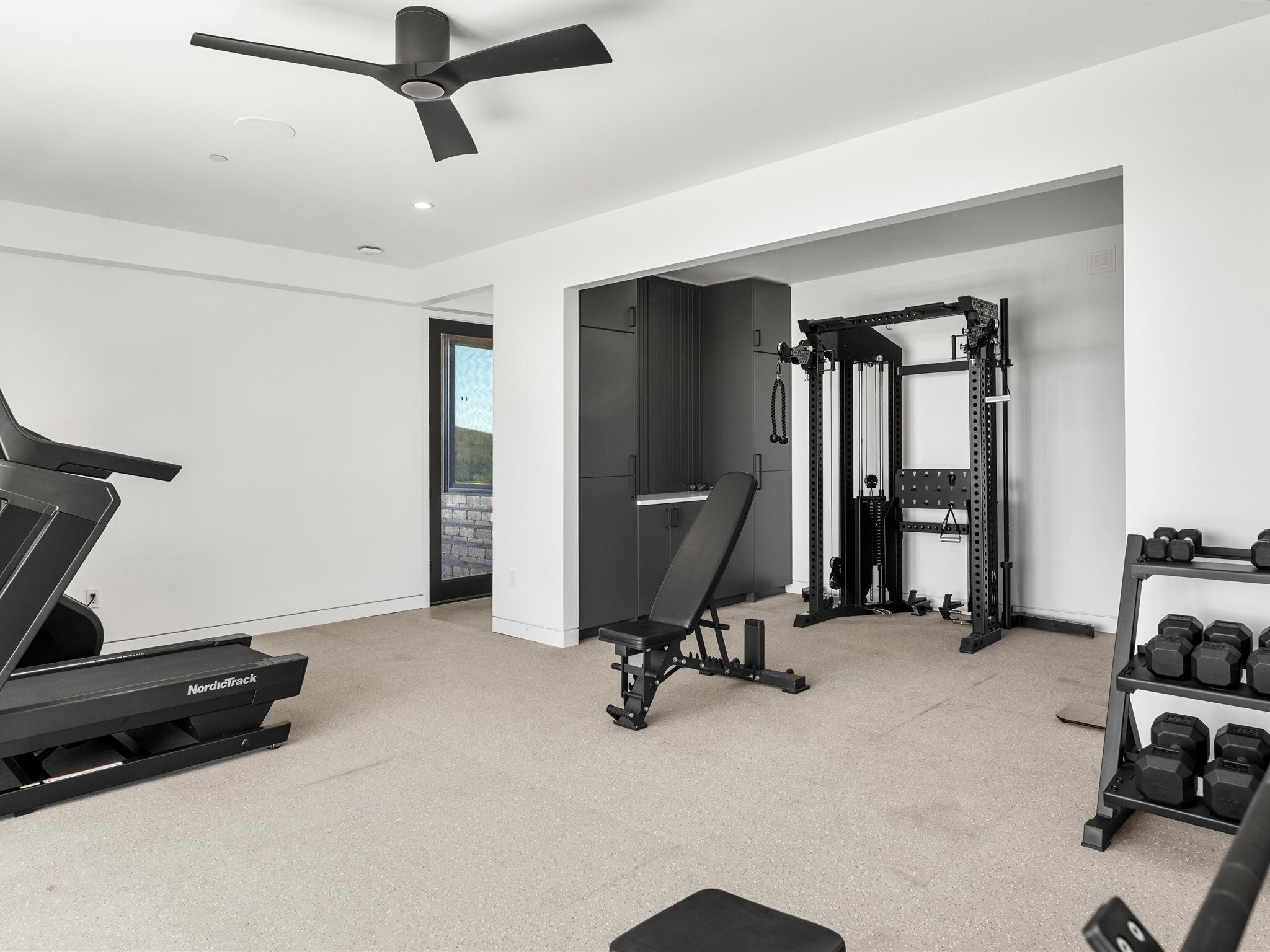 Une salle de sport moderne pour la maison, équipée d’un tapis de course, d’un banc de musculation, d’un support à squats et d’haltères.