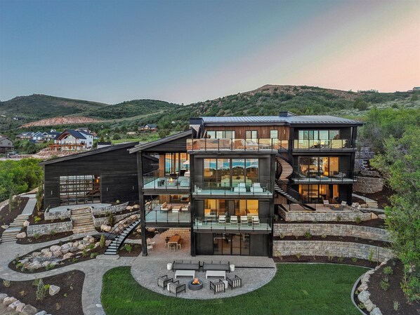 A modern multi-story house with a glass facade, outdoor seating, and a stone retaining wall.