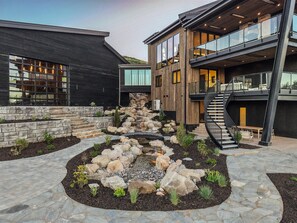 A modern building with a stone pathway leading to a wooden deck, a staircase, and a small garden area.