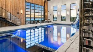 Una piscina interior con vistas a montañas a través de amplias ventanas, una escalera y una pared de madera.