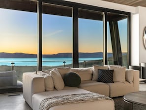 A modern living room with a sofa, a coffee table, and a view of a body of water and mountains.