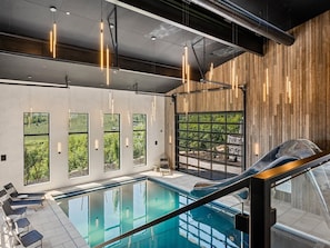 A modern indoor pool with a clear view of the outdoors, large windows, and a wooden wall.