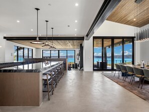 A modern kitchen with a large island, bar seating, and large windows offering a view of the outdoors.