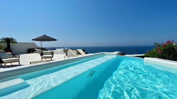 Una piscina con acqua cristallina, lettini prendisole e vista sull'oceano.