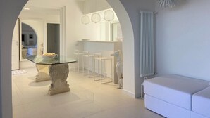 Un interno moderno con un tavolo da pranzo in vetro, sedie bianche, un divano bianco e una lampada decorativa a soffitto.