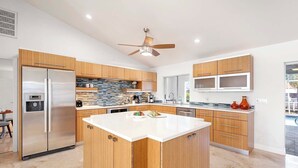 A modern kitchen with wooden cabinets, a stainless steel refrigerator, a central island, and a ceiling fan. - Allure - Luxury Rental in Walking Distance to Cape Coral Yacht Club (Cape Coral)