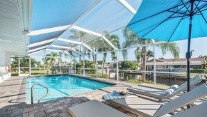 A pool area with a clear blue pool, lounge chairs, and umbrellas. - Allure - Luxury Rental in Walking Distance to Cape Coral Yacht Club (Cape Coral)