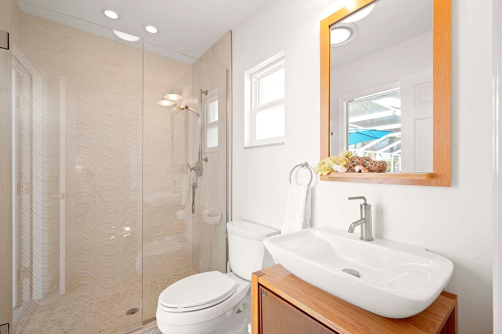 A modern bathroom with a glass-enclosed shower, a white toilet, and a wooden vanity with a sink.
