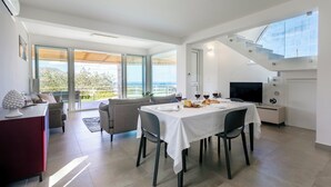 A modern dining area with a table set for two, a sofa, and a TV. - Villa dei Sospiri 4, Emma Villas (Castellammare del Golfo)