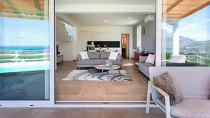 A modern living room with a sofa, coffee table, and a view of the kitchen and balcony. - Villa dei Sospiri 4, Emma Villas (Castellammare del Golfo)