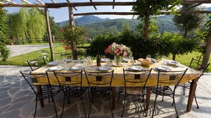An outdoor dining area with a table set for six, surrounded by chairs, set on a stone patio with a mountain view. - Villa Arbeio 8+6, Emma Villas (Genova)