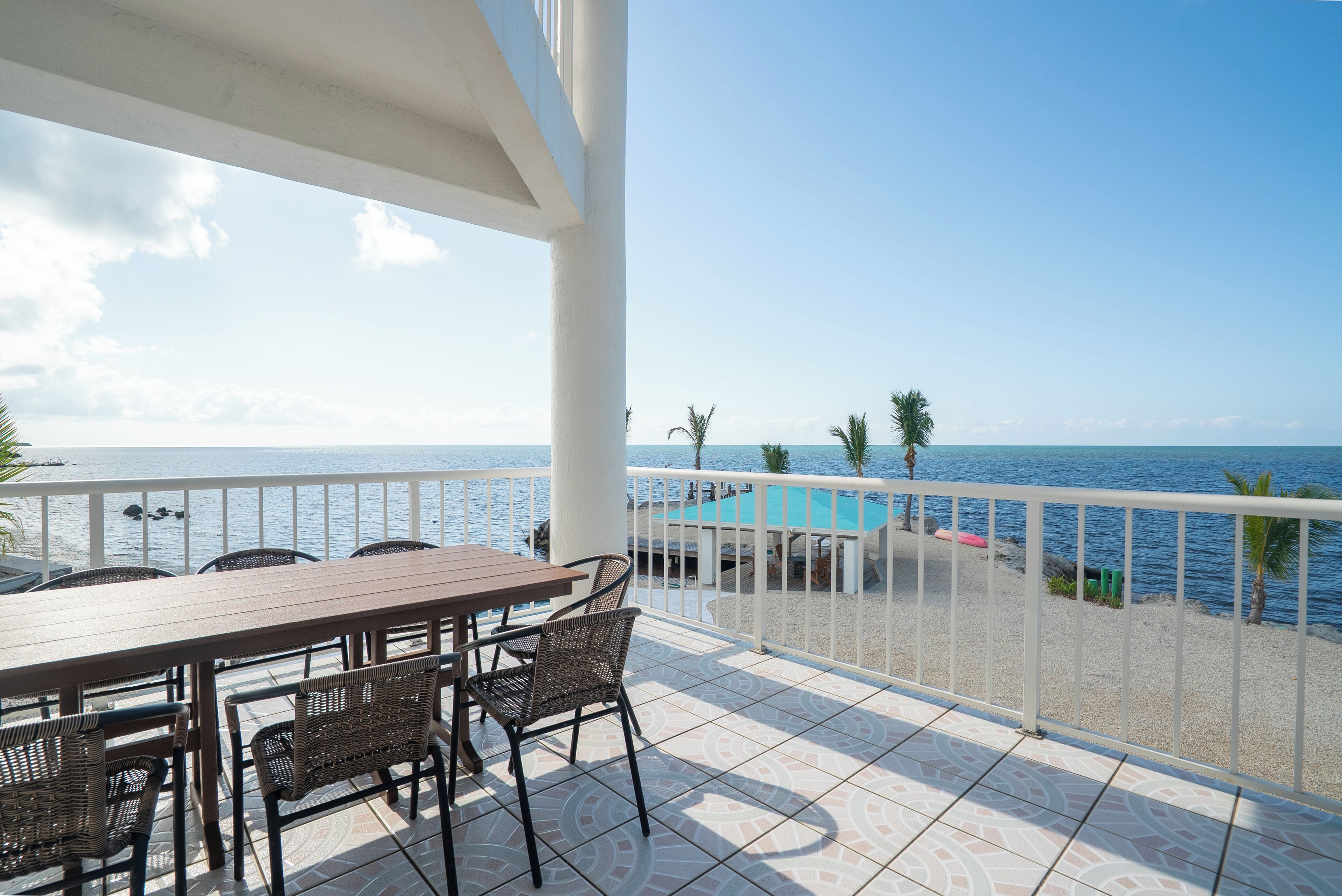 A terrace with a table and chairs, overlooking a pool and the sea.
