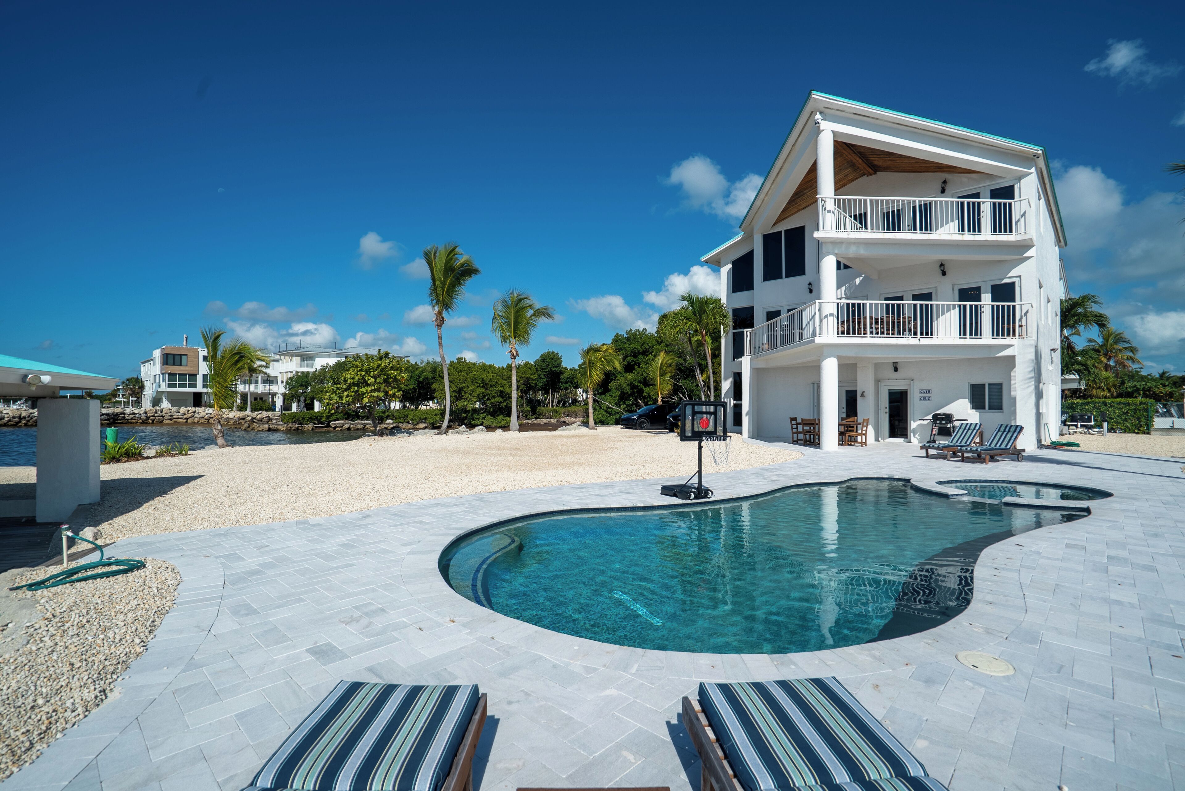 A modern two-story house with a swimming pool, lounge chairs, and a beach view.