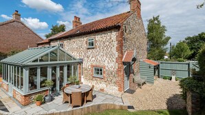 Ein Steinhhaus mit Wintergarten, Sitzgelegenheit im Freien und einer Steinsäule.