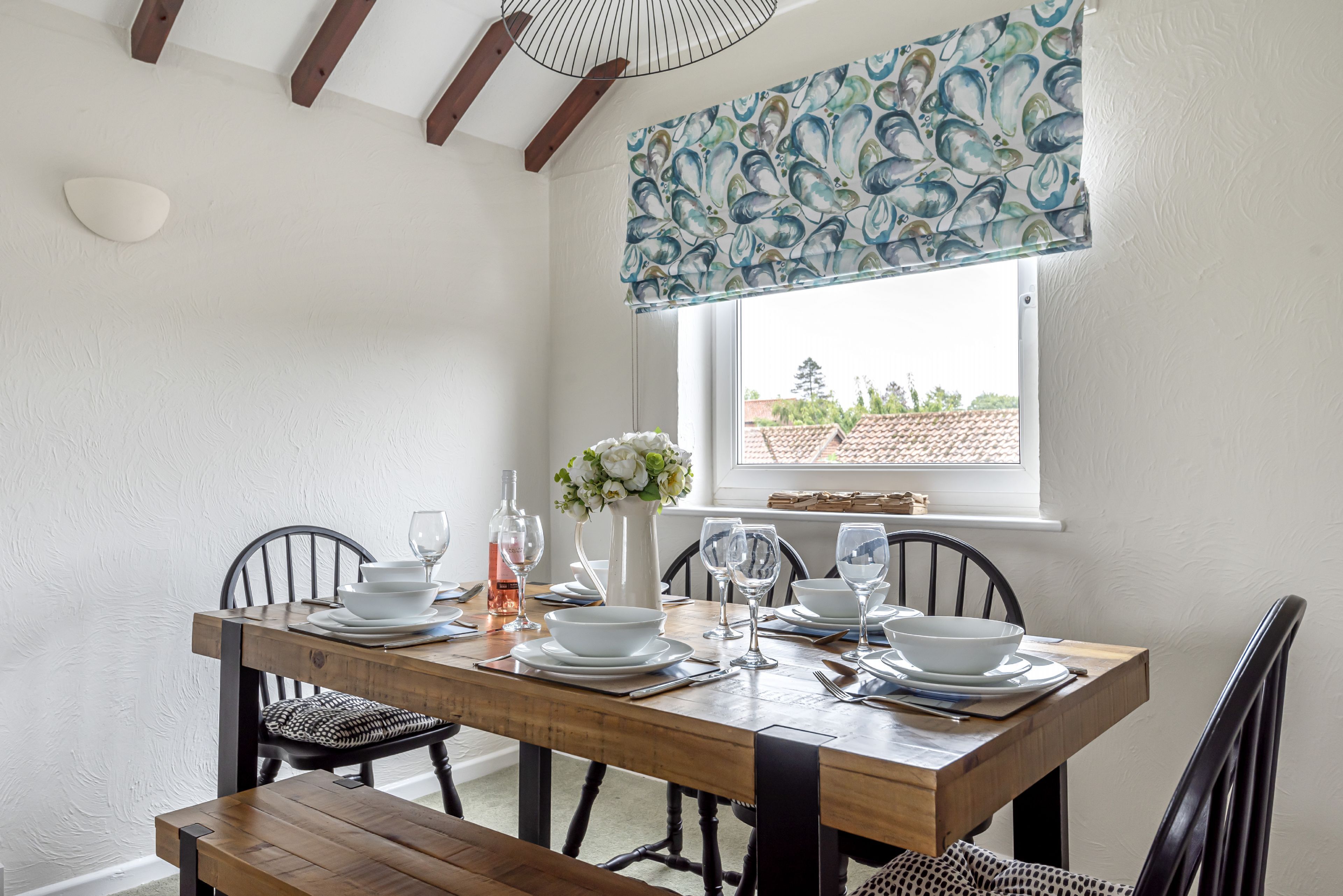 A dining area with a wooden table set for four, white walls, and a window with a view of buildings.