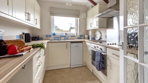 Una cocina compacta con armarios blancos, lavavajillas, horno y ventana que proporciona luz natural.