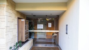 Corredor com mesa de recepção, porta de vidro e um pequeno espaço com plantas.