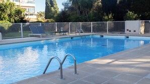 Uma piscina com deck revestido em azulejos, cerca branca e cadeiras de descanso.
