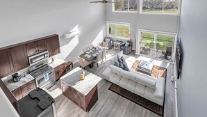 Une cuisine moderne avec des meubles de couleur bois foncé, un grand îlot central et un coin repas comprenant une table et des chaises blanches.