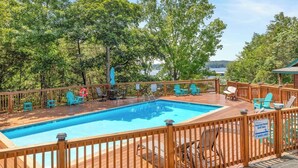 A wooden deck with a swimming pool, surrounded by trees and a view of the water. - Table Rock Lake Cabin - The Oaks #5 with Lake Access & Hot Tub (Shell Knob)