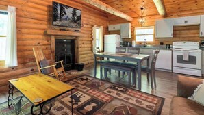 A log cabin interior with a dining area, kitchen, fireplace, and a large painting on the wall. - Table Rock Lake Cabin - The Oaks #5 with Lake Access & Hot Tub (Shell Knob)