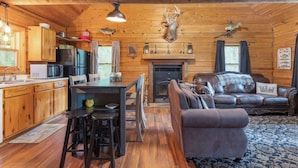 A cabin interior with a kitchen, dining area, and living room, featuring wooden walls, a fireplace, and mounted animal heads. - Table Rock Lake Cabin - The Cedars #1 with Lake Access, Hot Tub, Outdoor Pool (Shell Knob)