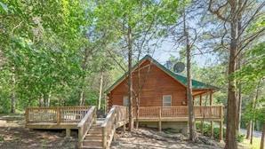 A wooden cabin with a deck and stairs, surrounded by trees. - Table Rock Lake Cabin - The Cedars #1 with Lake Access, Hot Tub, Outdoor Pool (Shell Knob)