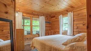 Camera da letto in una baita di legno con due letti, una scrivania in legno e una finestra con tende.