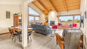 A spacious living area with a high wooden ceiling, a fireplace, and large windows offering a view of the outdoors. - Pacific FantaSea - Sea Ranch 2BR+Loft, Hot Tub, 6 (Sea Ranch)
