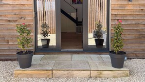 Exterior de fusta amb una porta corredissa de vidre, plantes en testos i una escala que condueix a un nivell superior.