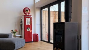 Habitació amb un sofà modern, una bomba de gas vermella, un bressol de fusta negra i un pont de fusta visible a través de la porta de vidre.