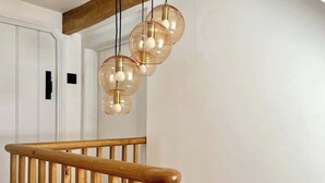 Eine Holztreppe mit Handlauf und einer modernen Pendelleuchte mit klaren Glaslampenschirmen und freiliegenden Glühbirnen.