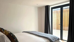 Quarto com uma cama grande, um cobertor cinza e vista para um deck de madeira através de uma porta de correr de vidro.