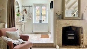 Een gezellige woonkamer met een open haard, een roze fauteuil en een uitzicht door een deuropening op een buitenruimte.