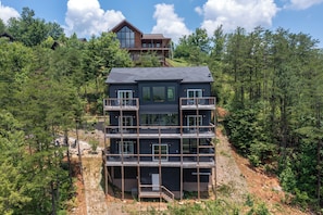 A multi-story building with balconies, surrounded by dense forest. - Modern Mountain Luxury 4BR 4.5BA with Indoor Pool and Incredible Views (Gatlinburg)