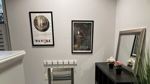 Una escalera con piso de madera oscura, barandal blanco y pared gris. Dos obras de arte enmarcadas se encuentran sobre el barandal y una consola negra con un espejo y pequeñas macetas.