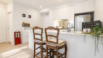 A modern kitchen with white cabinetry, a central island, two wooden bar stools, a red door, and a calendar on the wall.