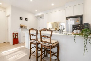 A modern kitchen with white cabinetry, a central island, two wooden bar stools, a red door, and a calendar on the wall.