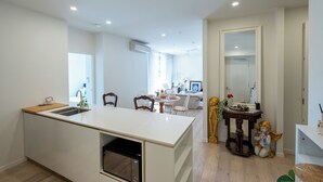 A modern kitchen with a central island, a dining area with a round table, and a living room with a sofa and chairs. - Artsy 2BR 2BA Retreat in West Village, West End Brisbane (West End)